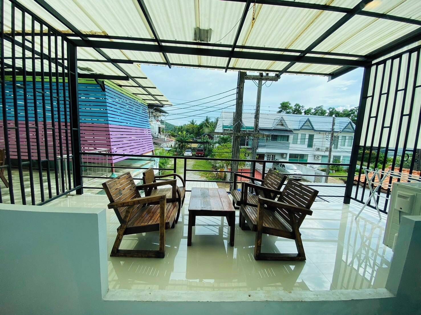 A covered outdoor seating area with wooden furniture and a view of colorful buildings in the background.
