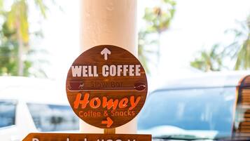Un cartel direccional con múltiples flechas indicando varios lugares como Well Coffee, Homav Coffee & Snacks, Bangkok a 462 Km, Área de Desayuno, U&I MiniMart, Habitaciones 101-102 y Lavandería.