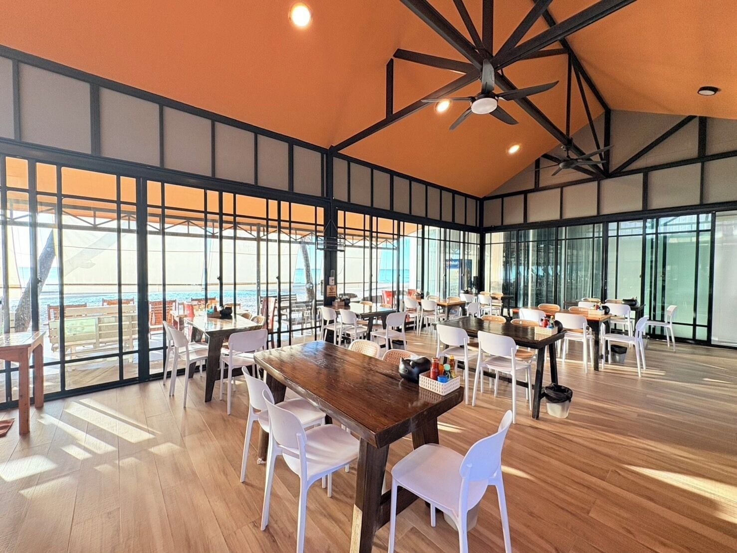 A spacious indoor area with multiple tables and chairs, large windows, and a ceiling fan.