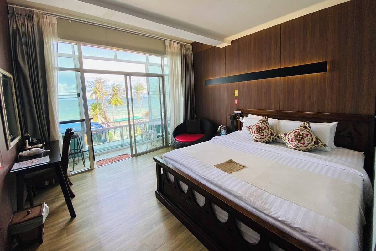 Ein Hotelzimmer mit einem großen Bett, einem Schreibtisch, einem Stuhl und Blick auf das Meer.