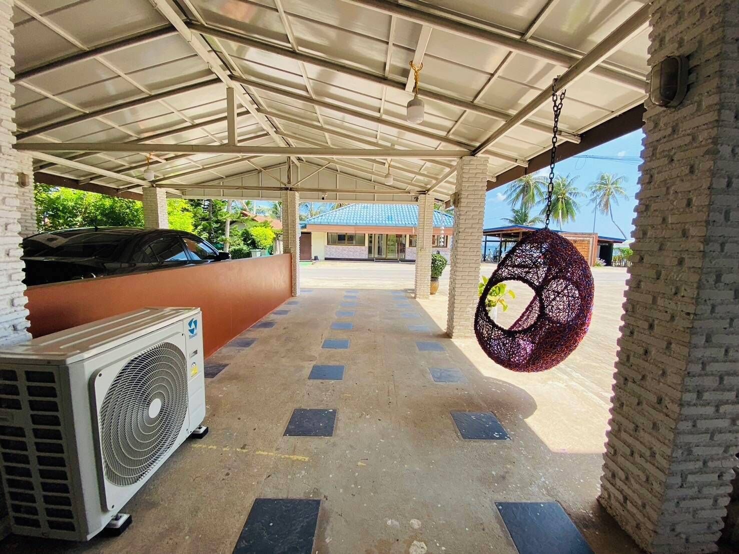 Un espace de stationnement extérieur abrité, doté d’un sol en béton, où se trouve une voiture garée et une grande unité de climatisation.