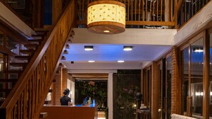 Um saguão de hotel com escadaria de madeira, balcão de recepção, um grande aquário e um sofá.