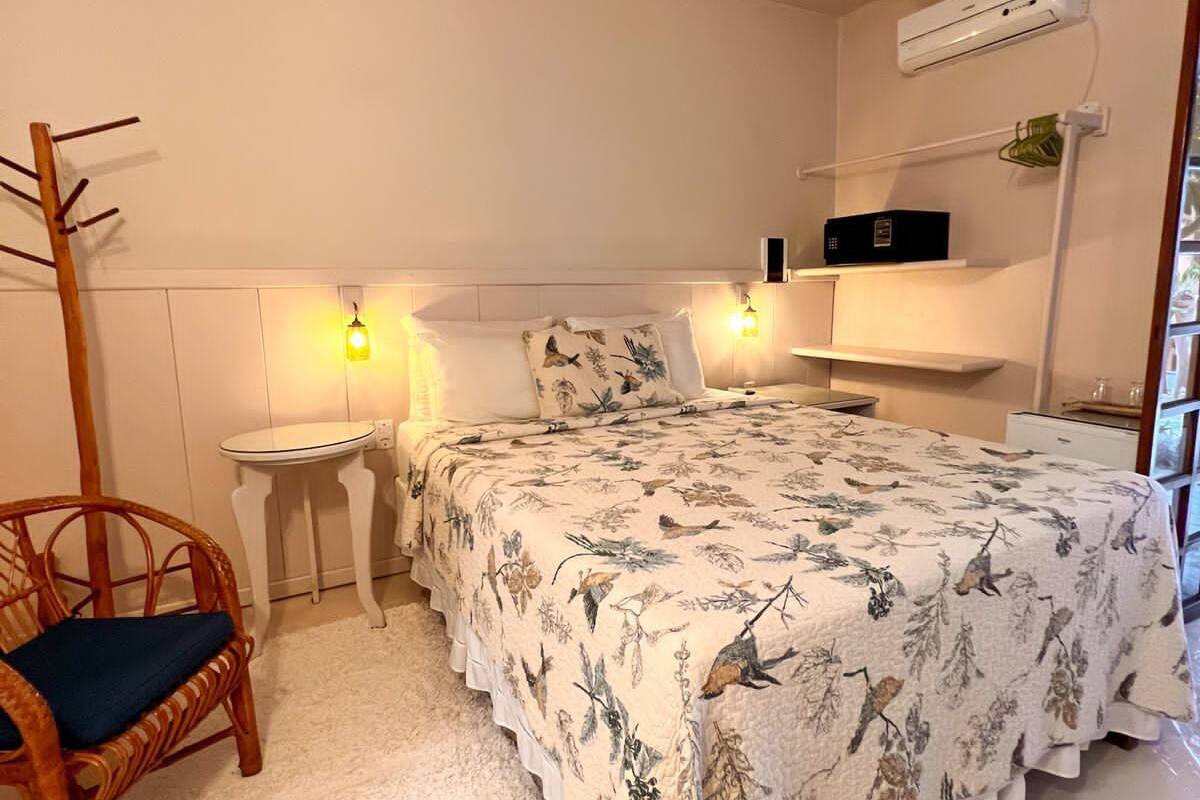 A bedroom with a bed, a chair, a small table, a ceiling fan, and an air conditioning unit.