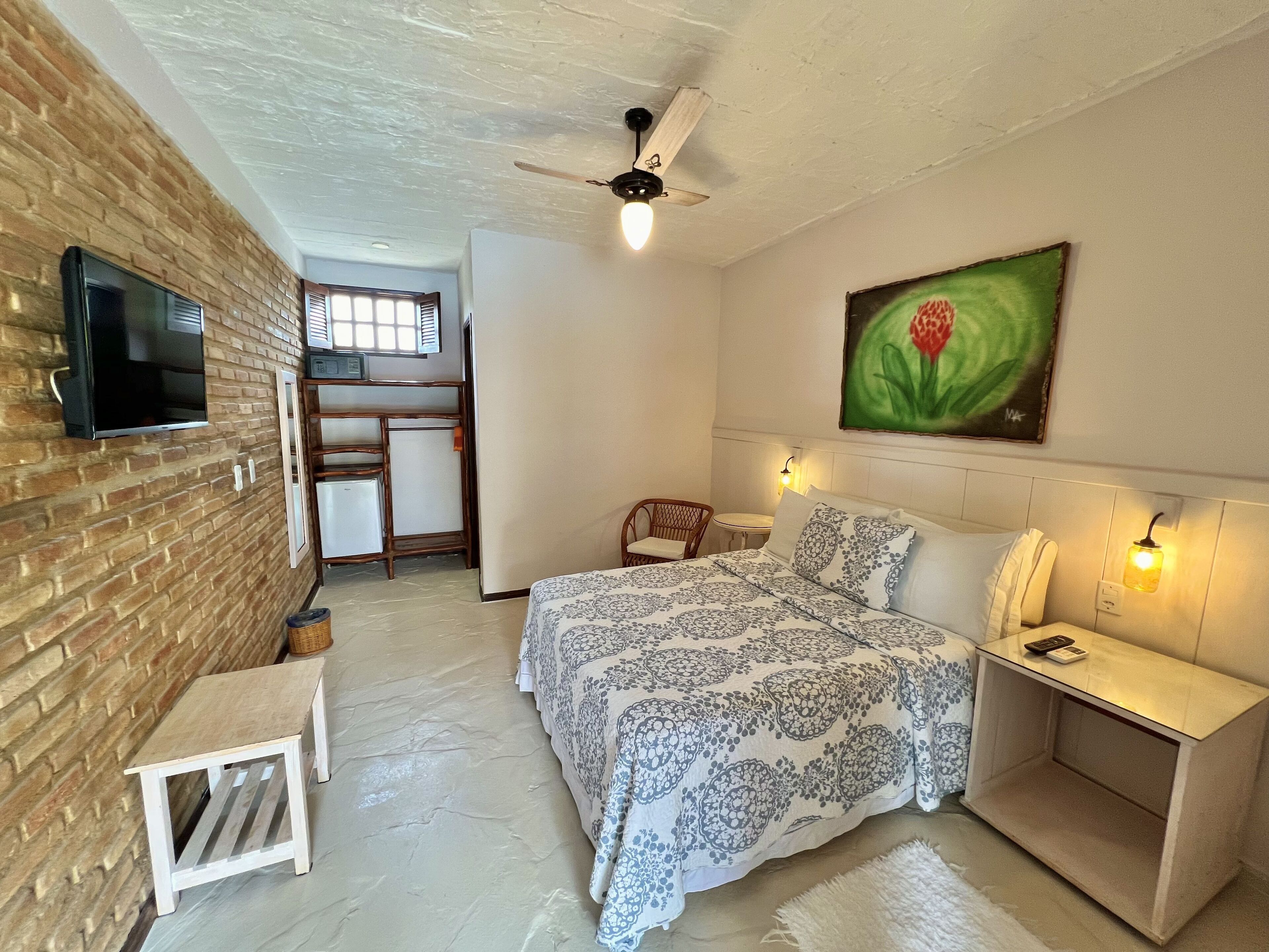 A bedroom with a bed, bedside table, and a television mounted on a brick wall.