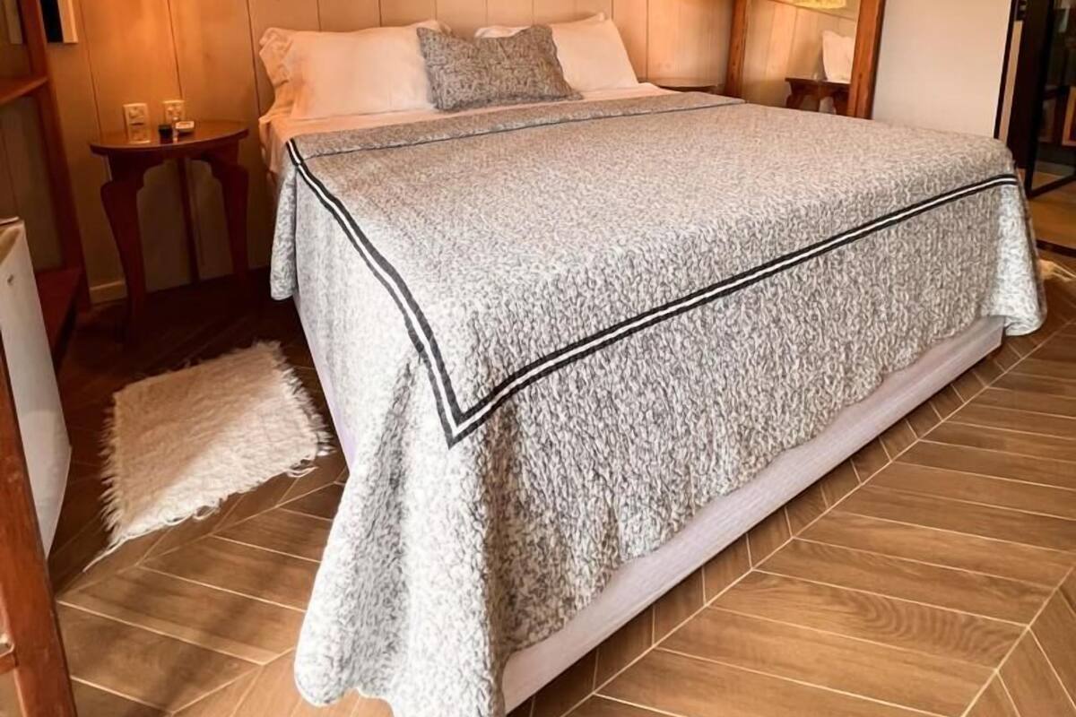 A bedroom with a large bed, wooden flooring, a ceiling fan, and wall-mounted lamps.