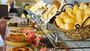 Buffet com diversos alimentos, incluindo pão, doces e sobremesas.