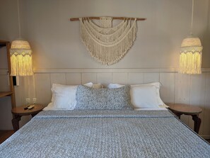 A bed with a patterned bedspread, two bedside tables, and macramé wall hangings. - Pousada Casa de Maria (Prado)