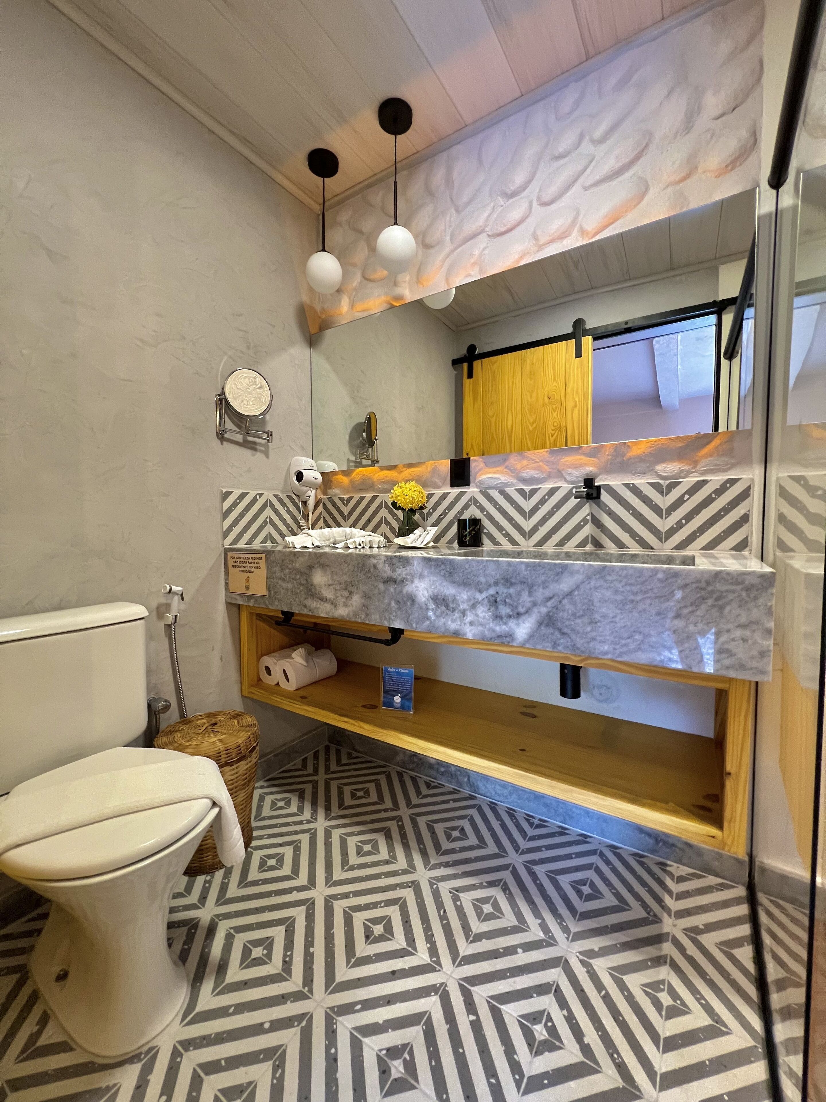 A bathroom with a toilet, a sink with a marble countertop, a shower area, and a patterned floor.