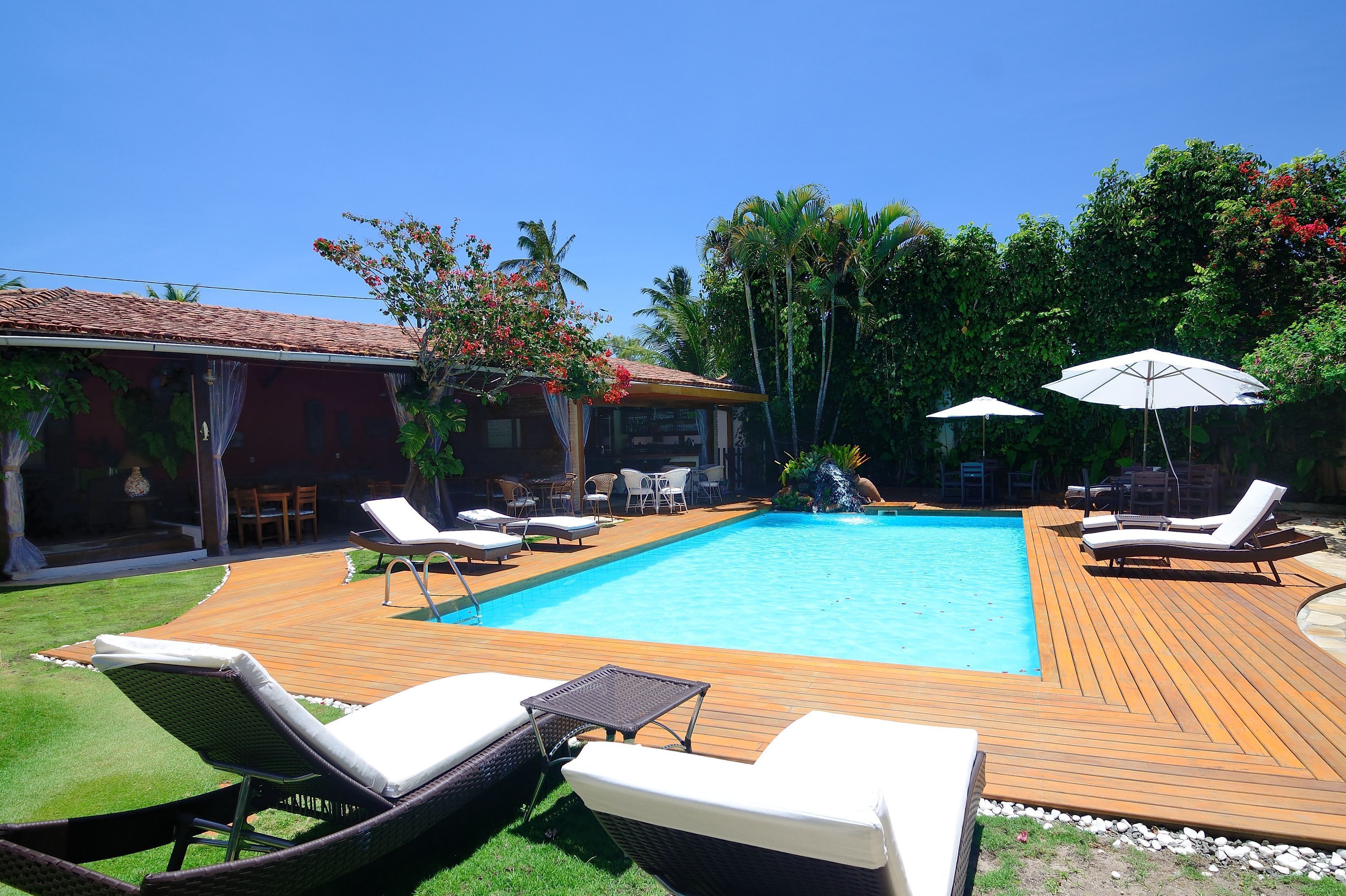 A swimming pool with lounge chairs and umbrellas, surrounded by a wooden deck and greenery.
