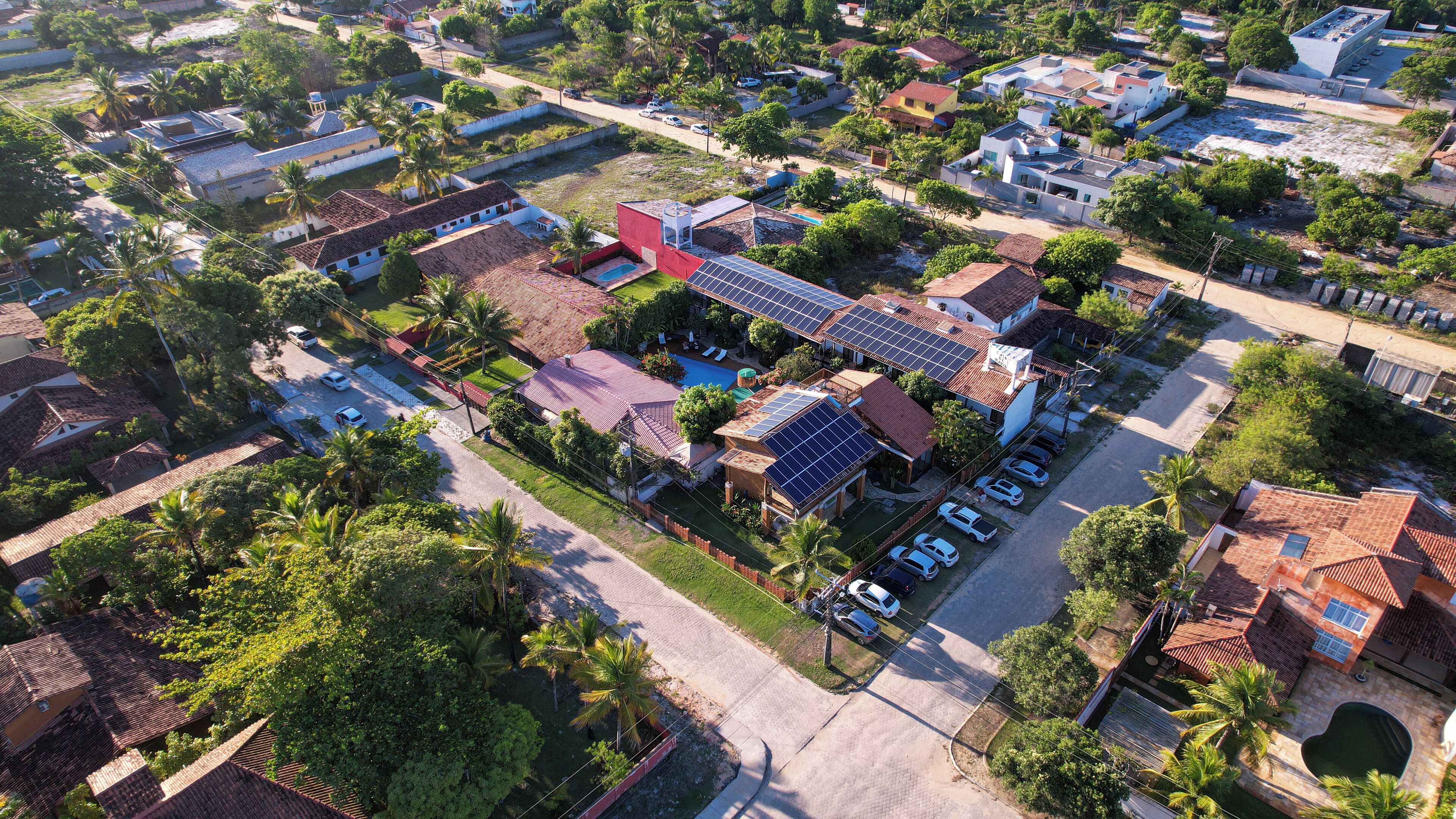 An aerial view of a residential area with houses, solar panels, and a swimming pool.