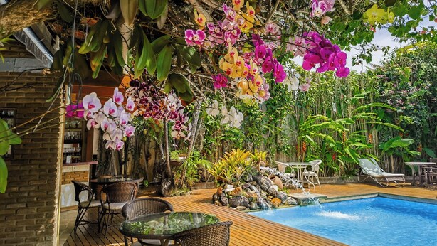 Uma área à beira da piscina com deck de madeira, espreguiçadeiras e um bar com mesas e cadeiras de vidro.