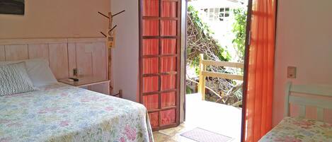 Un dormitorio con dos camas, un cabecero de madera, una mesita de noche y una puerta abierta que da al exterior.