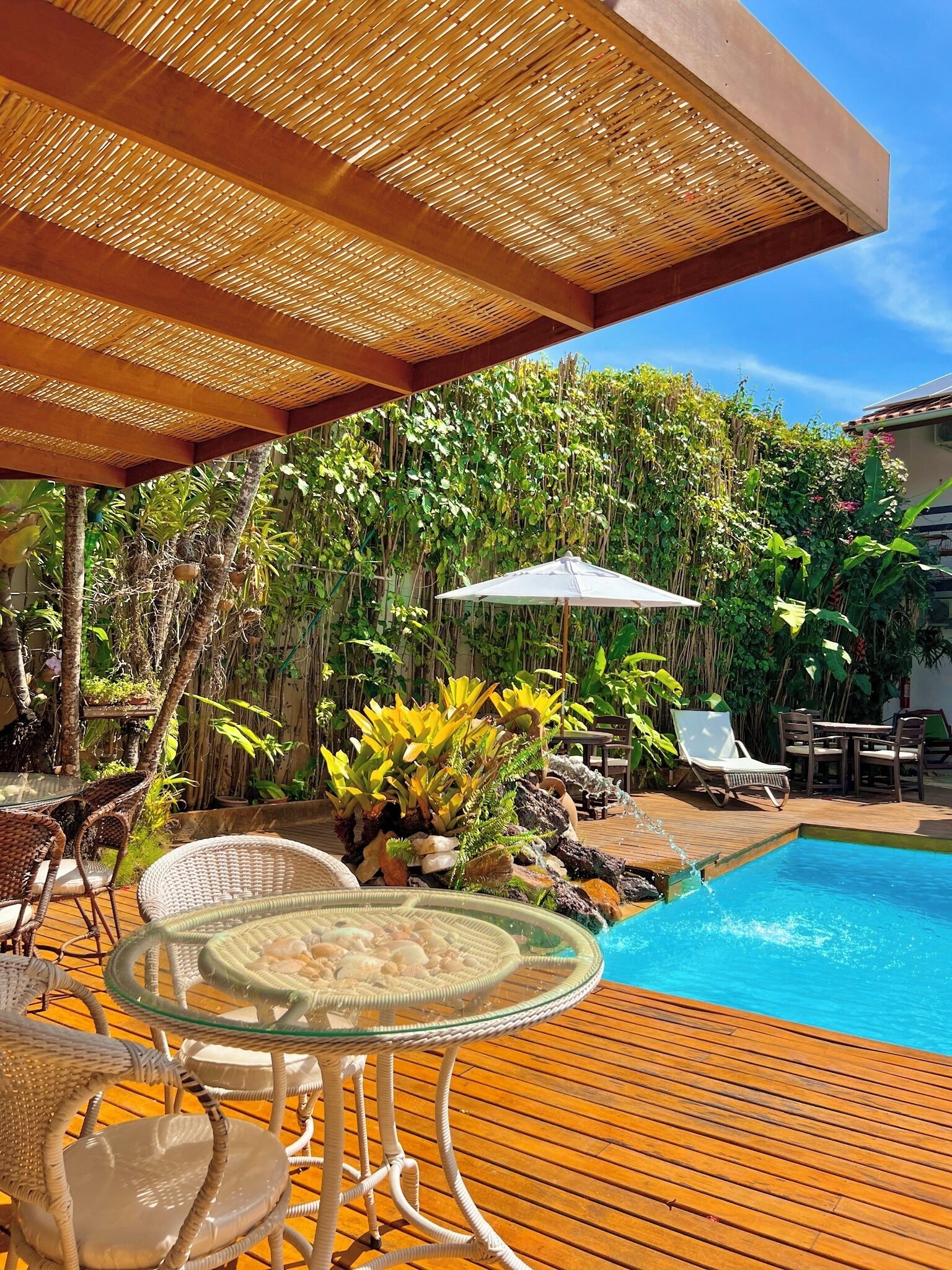 A wooden deck with a pool, surrounded by lush greenery and outdoor furniture.