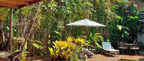 A wooden deck with a pool, surrounded by lush greenery and outdoor furniture.