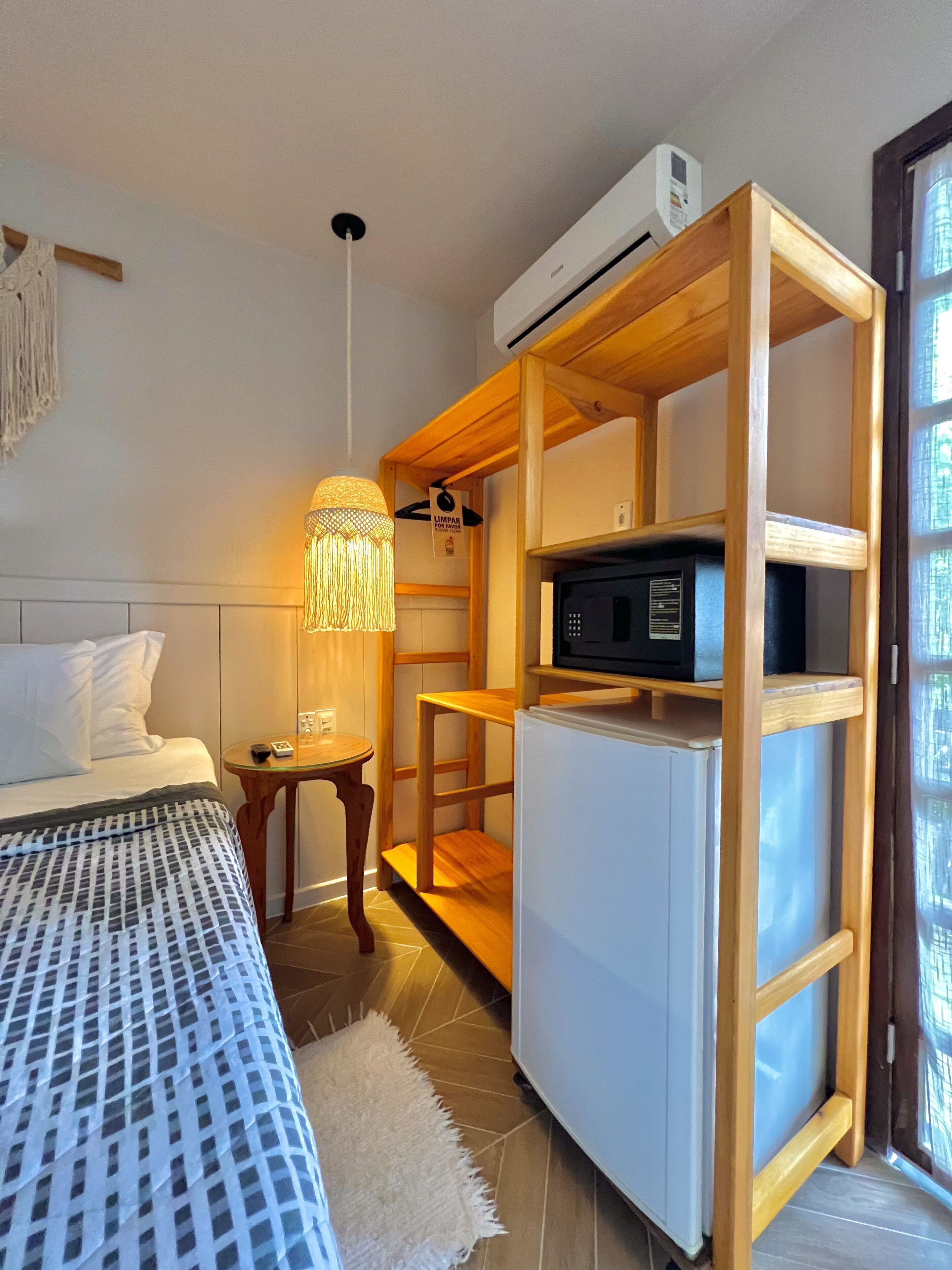A compact hotel room with a bed, a small table, a lamp, a microwave, and a refrigerator.