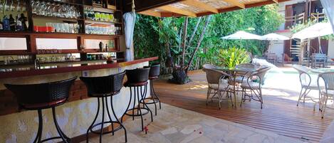 Un área de bar al aire libre con piso de piedra, taburetes de mimbre y sombrillas blancas.
