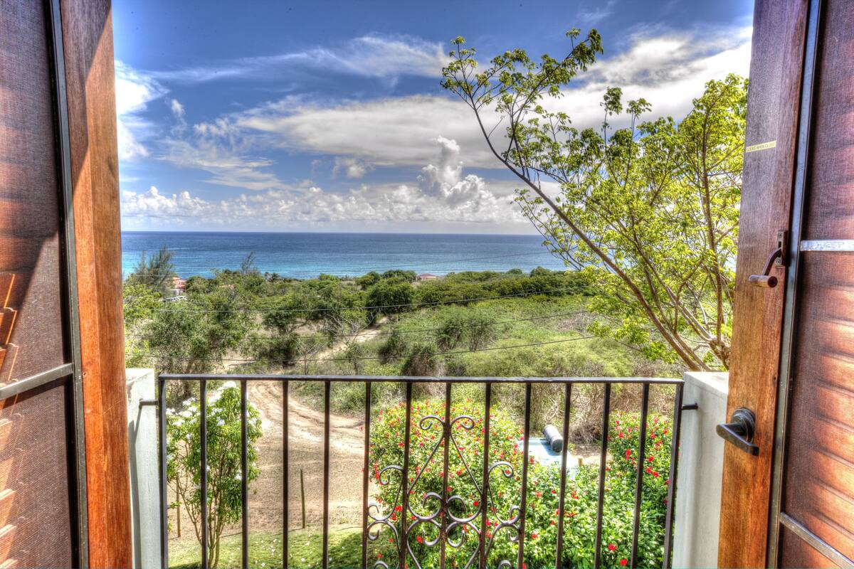Un balcon avec vue sur l’océan et la verdure.