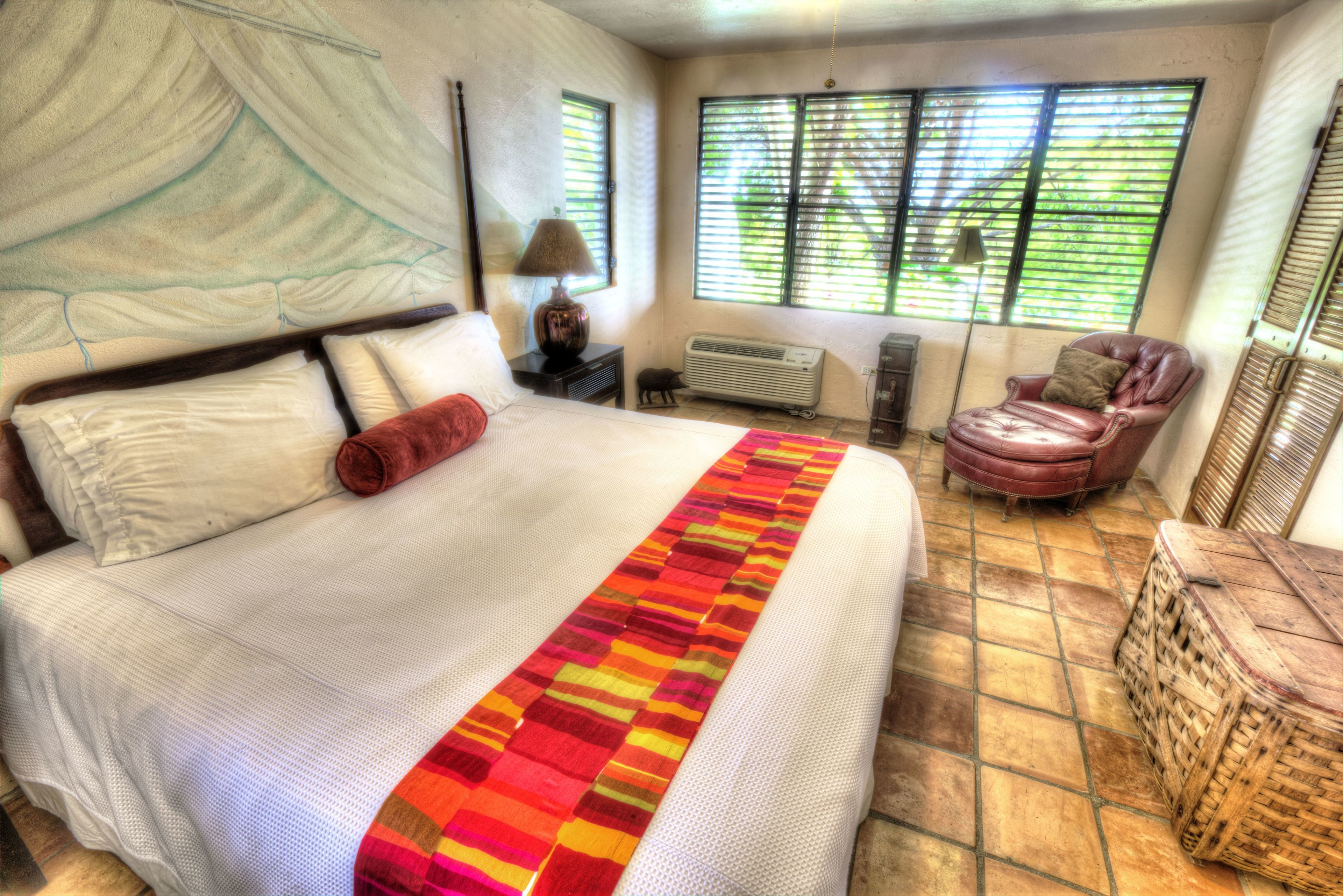 A bedroom with a large bed, a chair, a lamp, and a window with blinds.