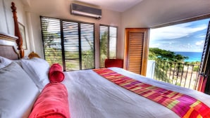 A hotel room with a large bed, a balcony with a view of the ocean, and a window with blinds. - Hacienda Tamarindo (Vieques)