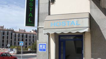Un edificio con un letrero que dice "HOSTAL" y una puerta azul, que indica que es un albergue. Hay dos plantas en macetas al frente.