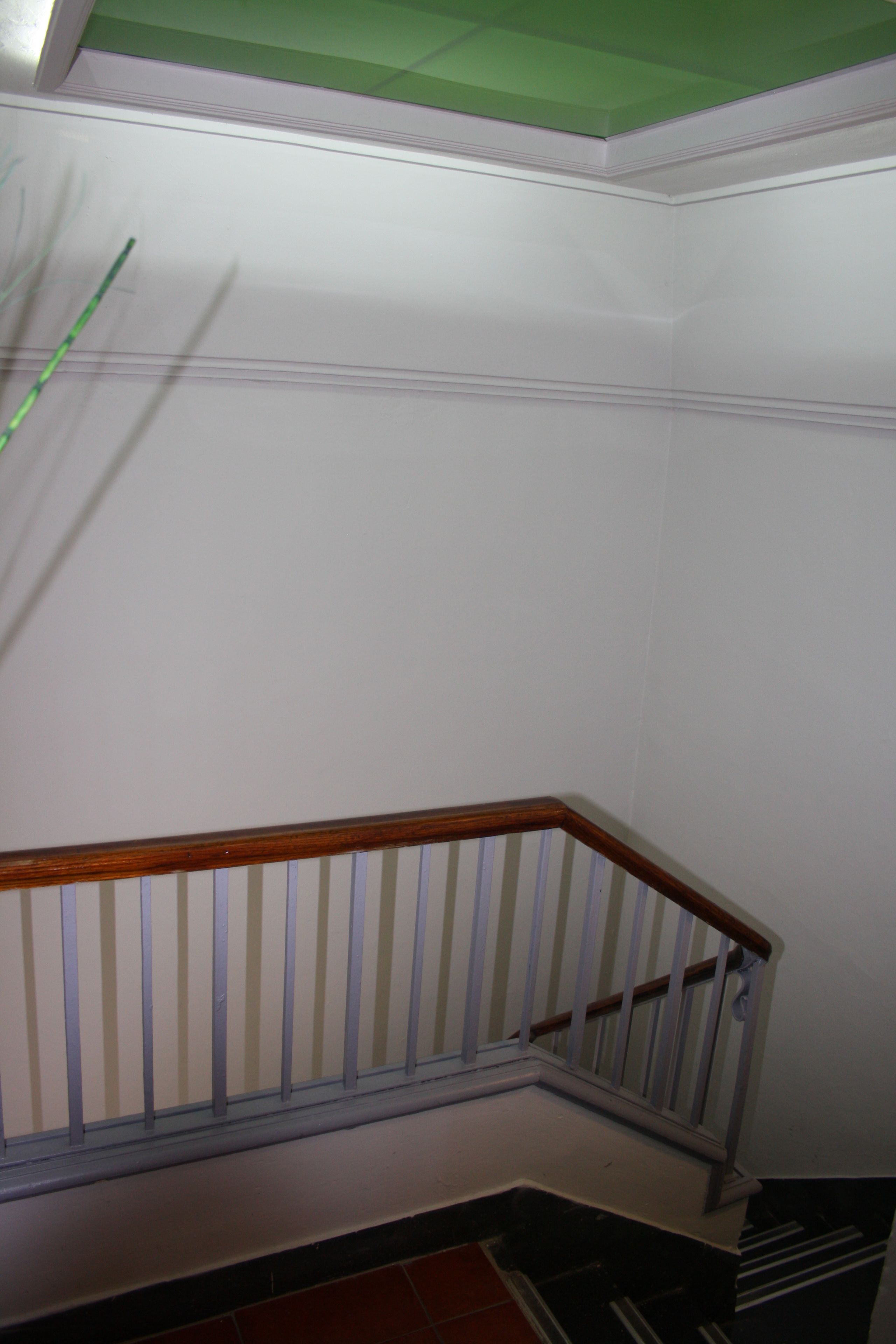 Een trap met een houten leuning en witte spijbels, die uitkomt op een vloer met een groen plafond.
