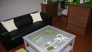 A living room with a glass-top coffee table, a black leather sofa, and a wooden cabinet.