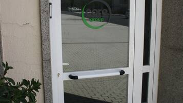 Una puerta blanca con un panel de vidrio y un pomo, ubicada en una esquina con una planta pequeña a un lado.