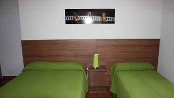 Habitación de hotel con dos camas individuales, cabecero de madera, mesita de noche con lámpara y un cuadro colgado en la pared.