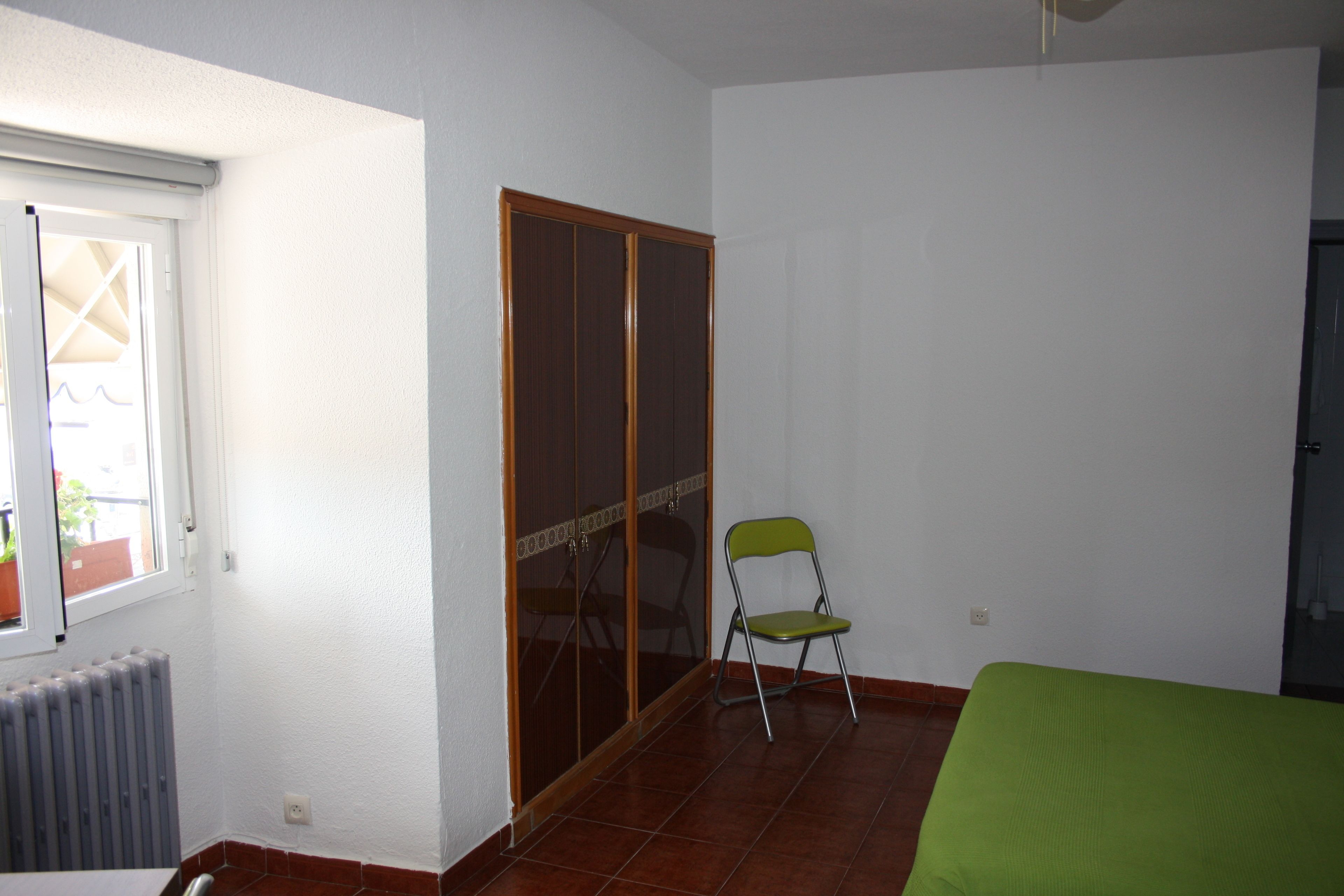 A room with a sliding door closet, a radiator, a green chair, and a bed with a green bedspread.