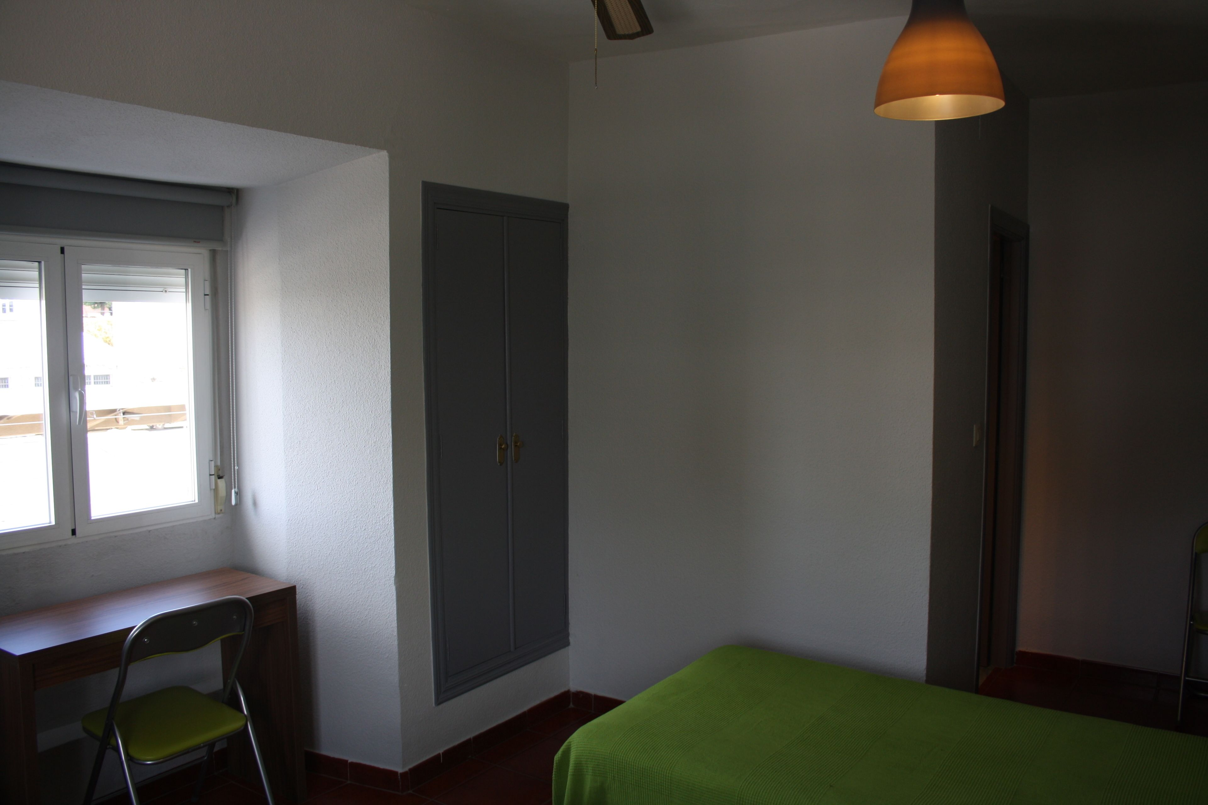 Una habitación con escritorio, silla, cama, armario y ventana.