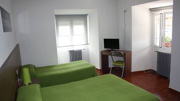 Una habitación con dos camas, un escritorio con silla, una ventana y un radiador.