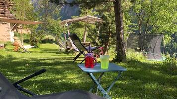 Ein Campingplatz mit Tisch und Stühlen, einem Zelt und einer Holzhütte in einer Berglandschaft.