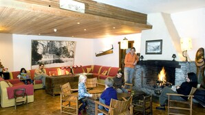 A cozy lounge area with wooden furniture, a fireplace, and a large painting on the wall. - Les Chalets du Villard (Saint-Veran)