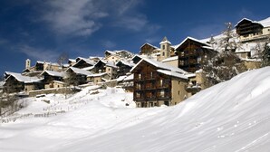 A snow-covered mountain village with traditional wooden buildings, a ski slope, and a clear blue sky. - Les Chalets du Villard (Saint-Veran)