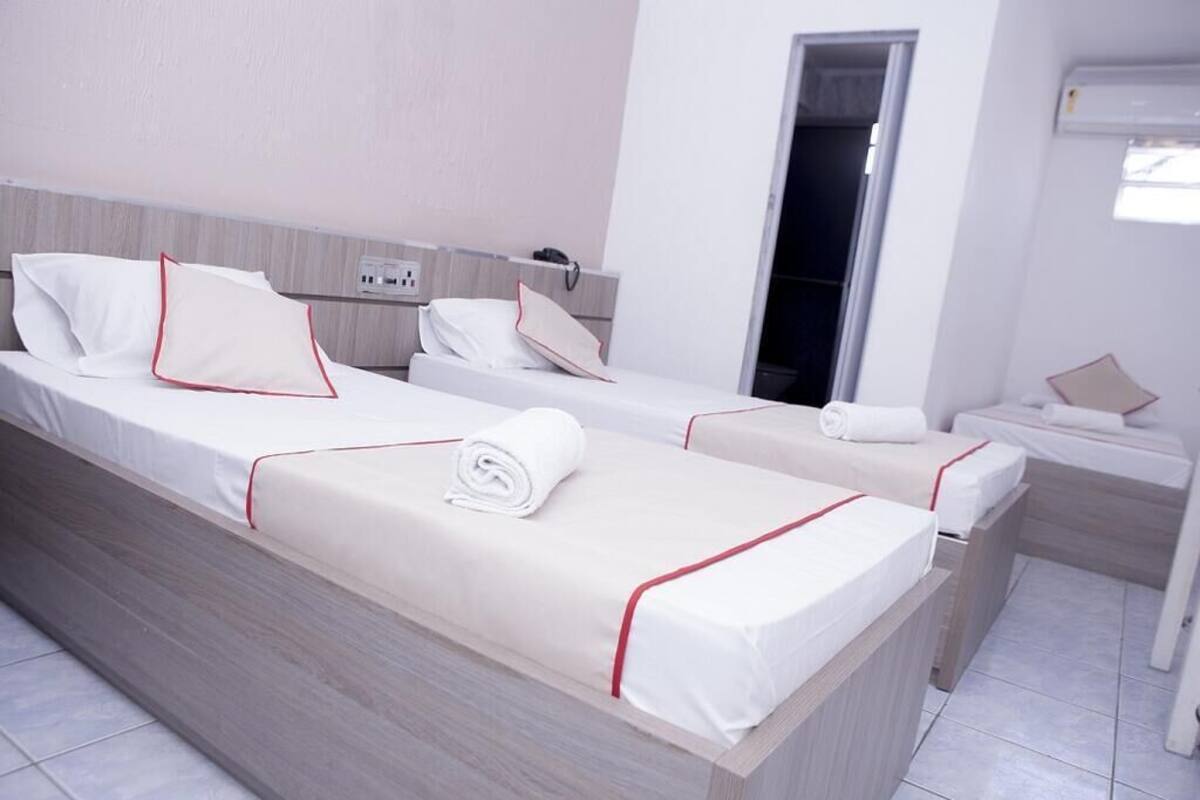 A hotel room with two beds, each with white linens and red trim, a bedside table, and a small nightstand.
