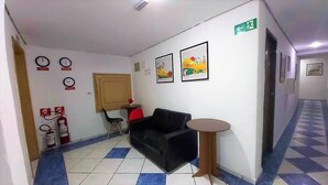 A lobby with a black sofa, a small round table, a fire extinguisher, and a door with an exit sign.