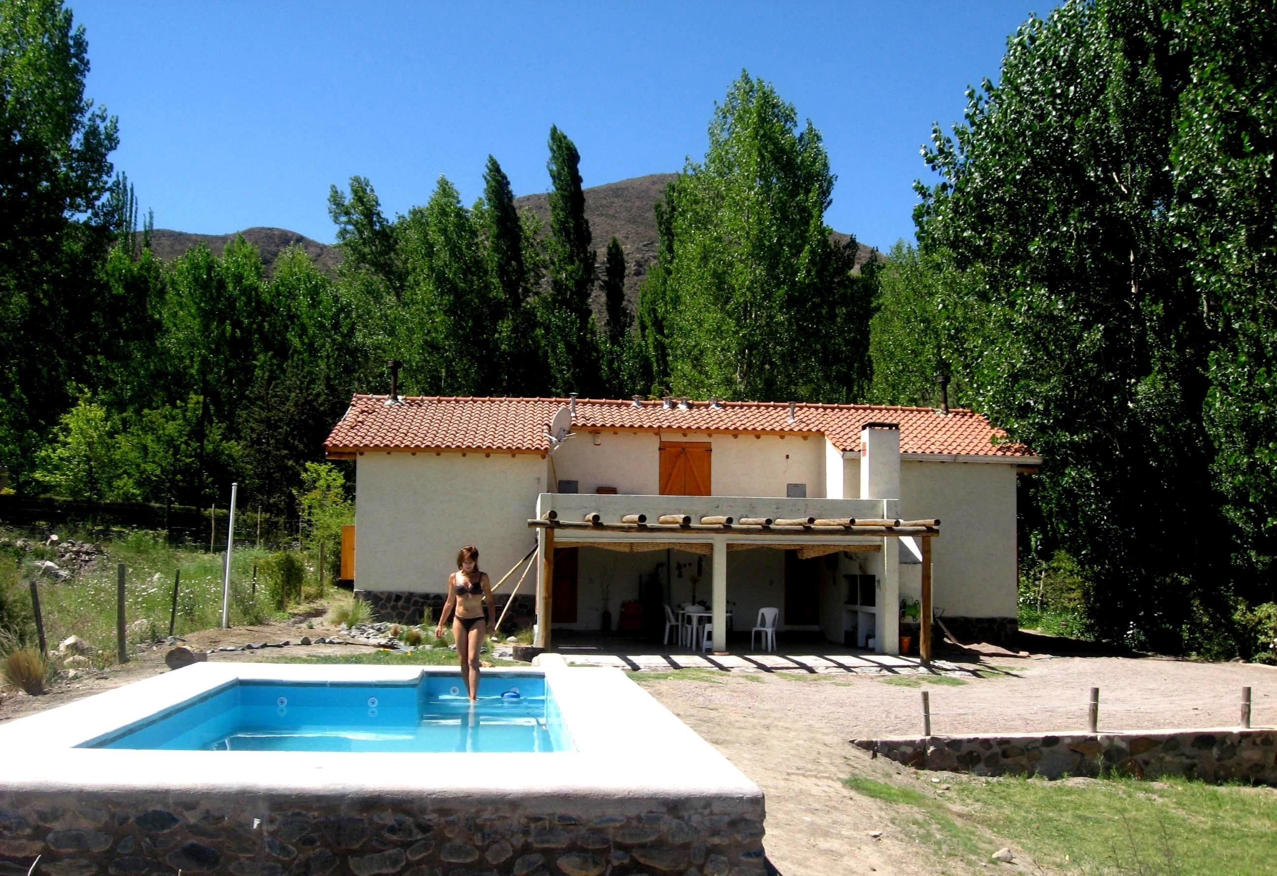 Una piscina con bordo in pietra, una zona patio coperta e una casa con tetto in tegole.