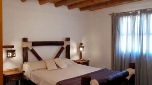 Une chambre à coucher avec une tête de lit en bois, un lit avec une literie blanche, deux tables de chevet avec des lampes et une fenêtre avec des rideaux.
