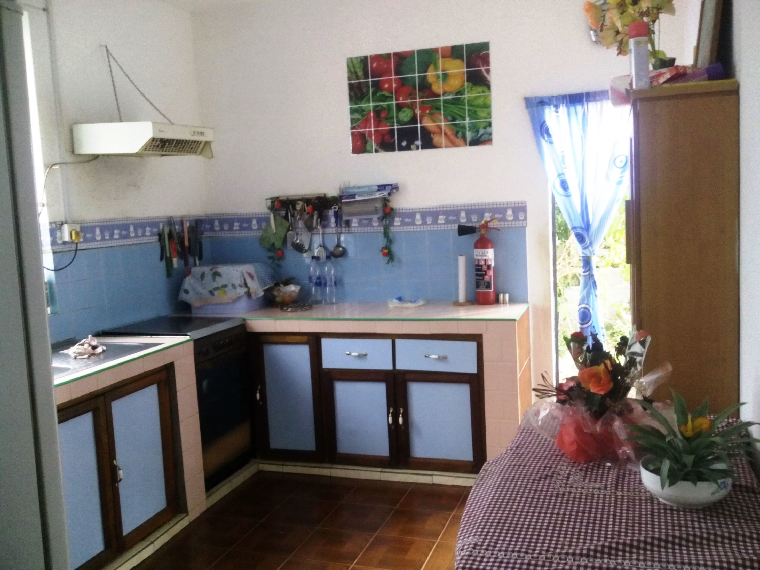 A compact kitchen with a tiled backsplash, a small dining area, and a window with curtains.