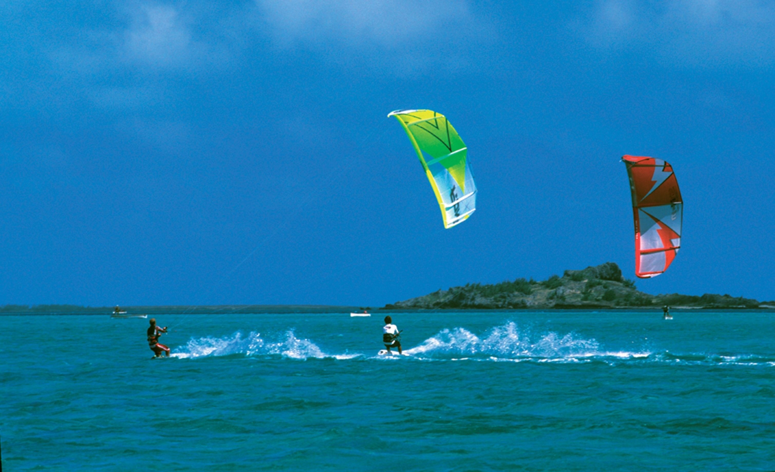 A coastal scene with two windsurfers and a distant island.