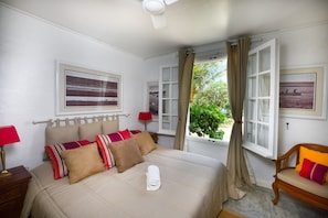 A neatly made bed with a rolled towel, two bedside tables with lamps, a window with curtains, and two framed pictures on the wall. - Chateau de Feuilles (Poste Lafayette)