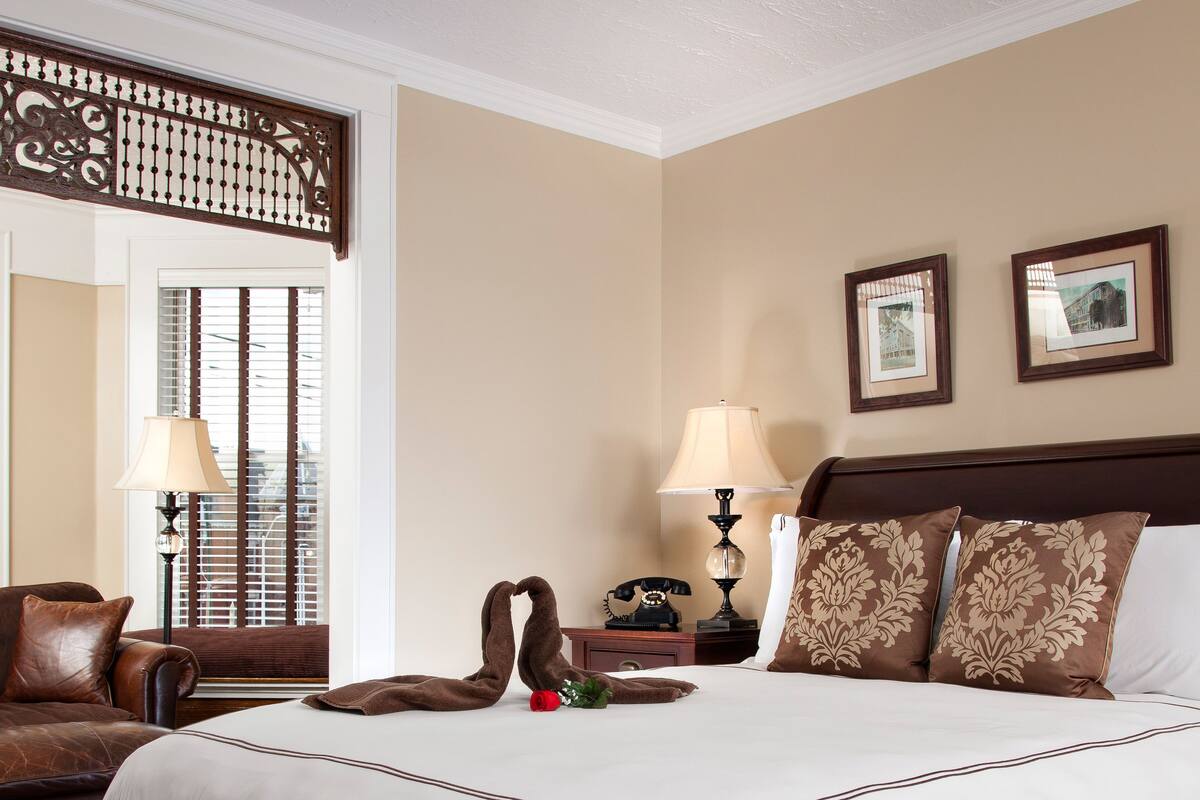 Habitación de hotel con una cama grande, cabecera de madera, dos lámparas de noche, un teléfono y un biombo decorativo.