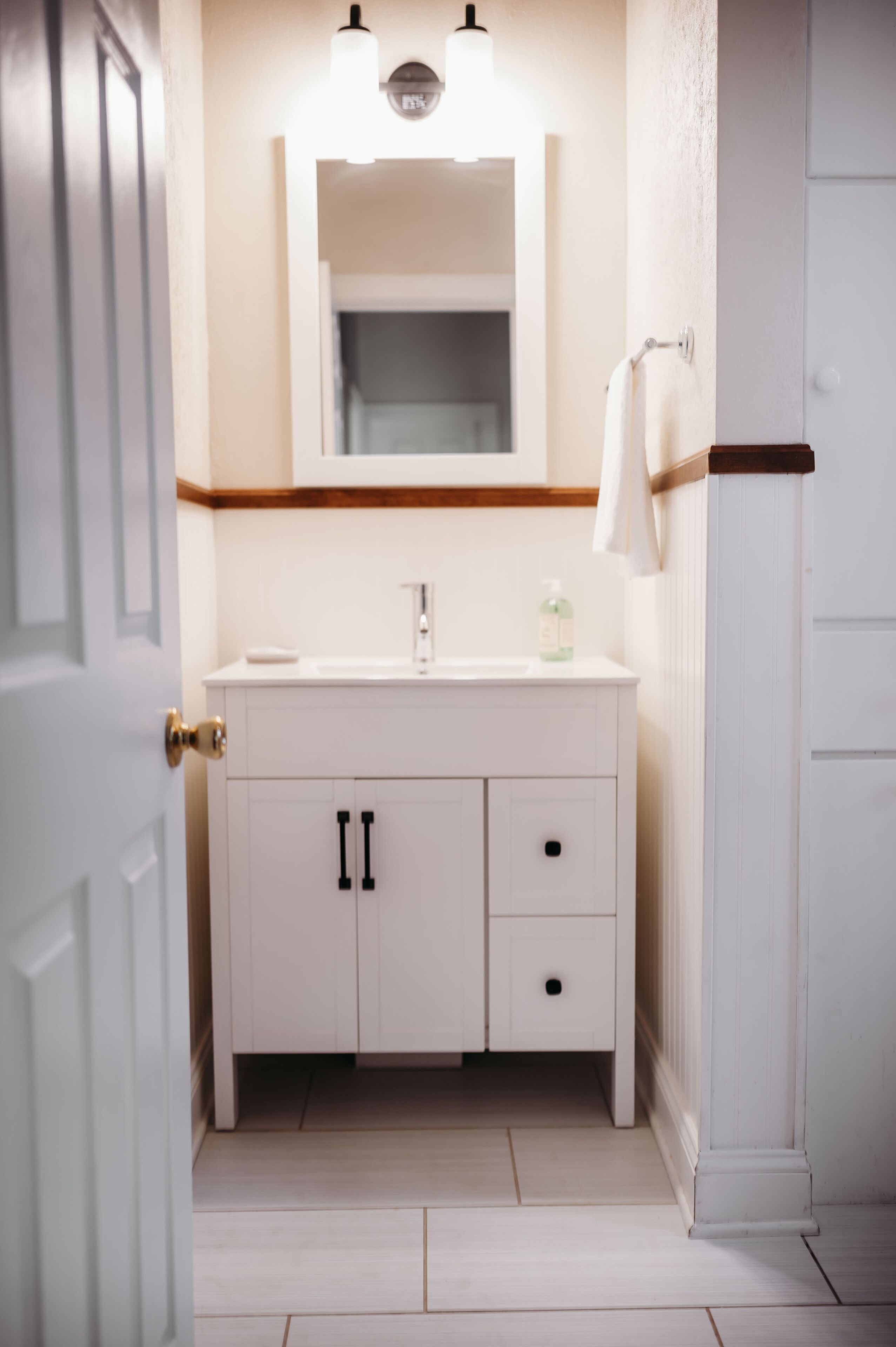 A bathroom with a white vanity, a mirror, and a towel hanging on the wall.