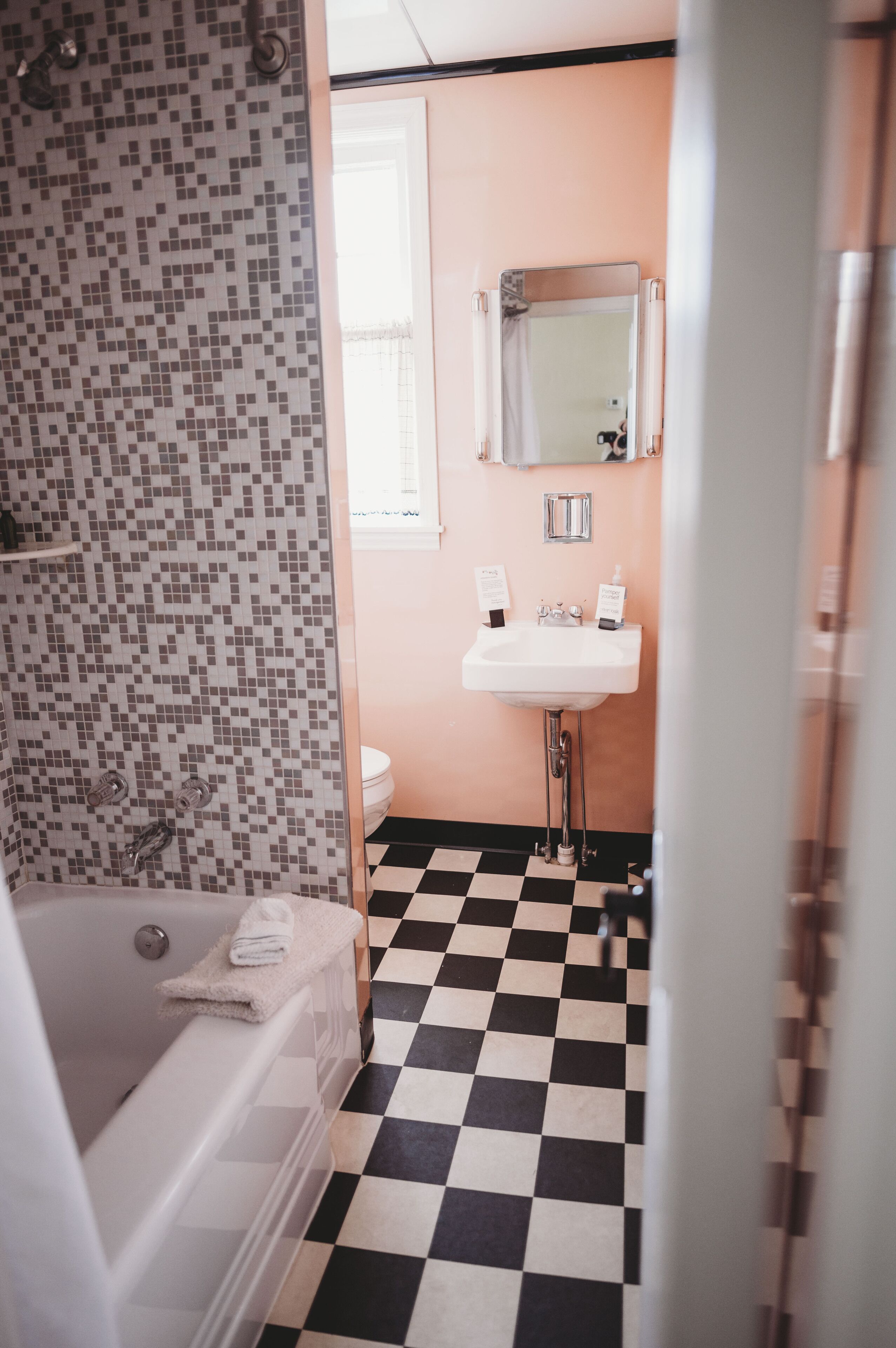A bathroom with a checkered floor, a tiled shower wall, a sink with a mirror, and a toilet.