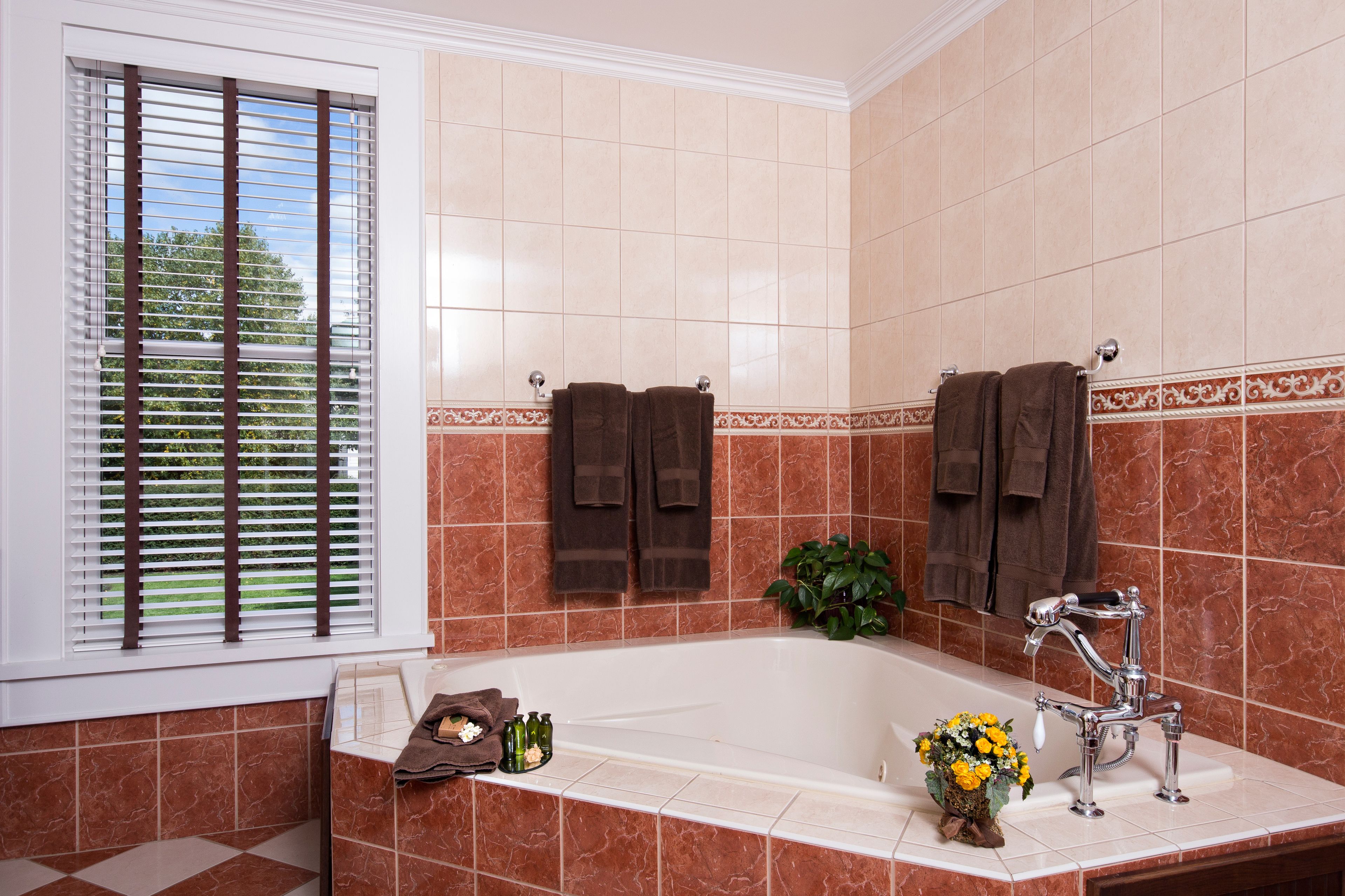 Un baño con bañera, dos toallas colgadas en la pared, una ventana con persianas y una planta a un lado.