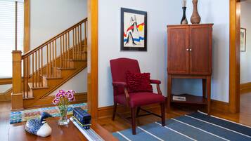 A living room with a wooden staircase, a red armchair, a wooden cabinet, and a framed artwork on the wall.