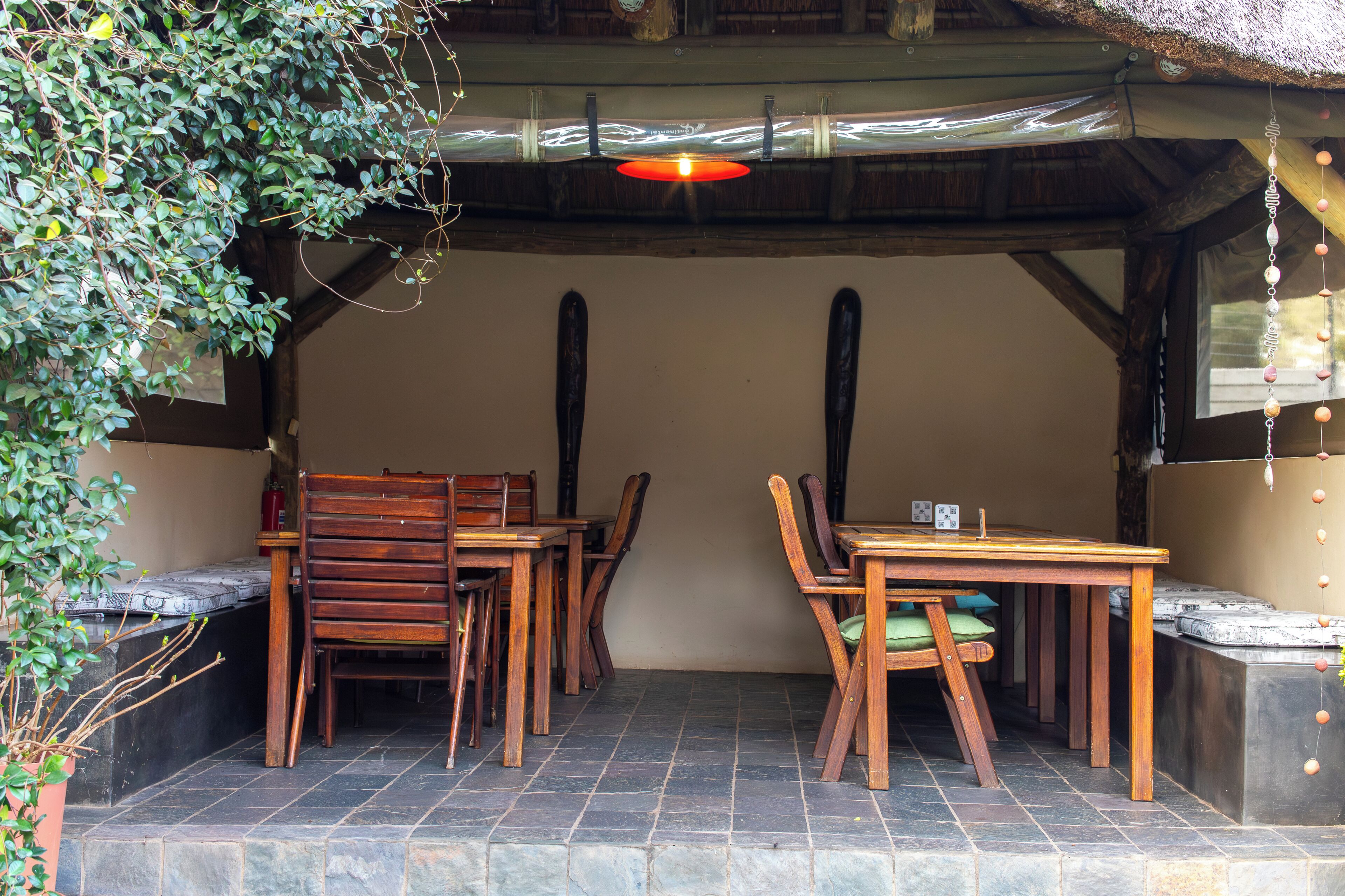 Een buiten eetgedeelte met houten tafels en stoelen, een rieten dak en stenen vloeren.