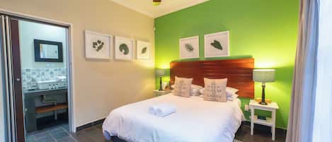 A hotel room with a bed, a nightstand, a lamp, a mirror, and framed artwork on the wall.