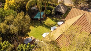 A residential area with a swimming pool, a thatched-roof structure, and a tiled-roof building. - Khayamanzi Guesthouse (Hartbeespoort)