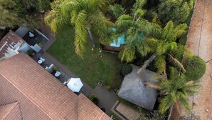 An aerial view of a property with a tiled roof, a swimming pool, and surrounding greenery including palm trees. - Khayamanzi Guesthouse (Hartbeespoort)